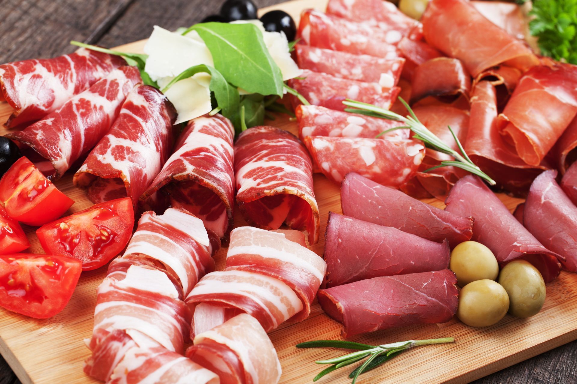 Assortiment de charcuteries, d'olives et de fromages sur une planche en bois avec des feuilles de basilic frais.