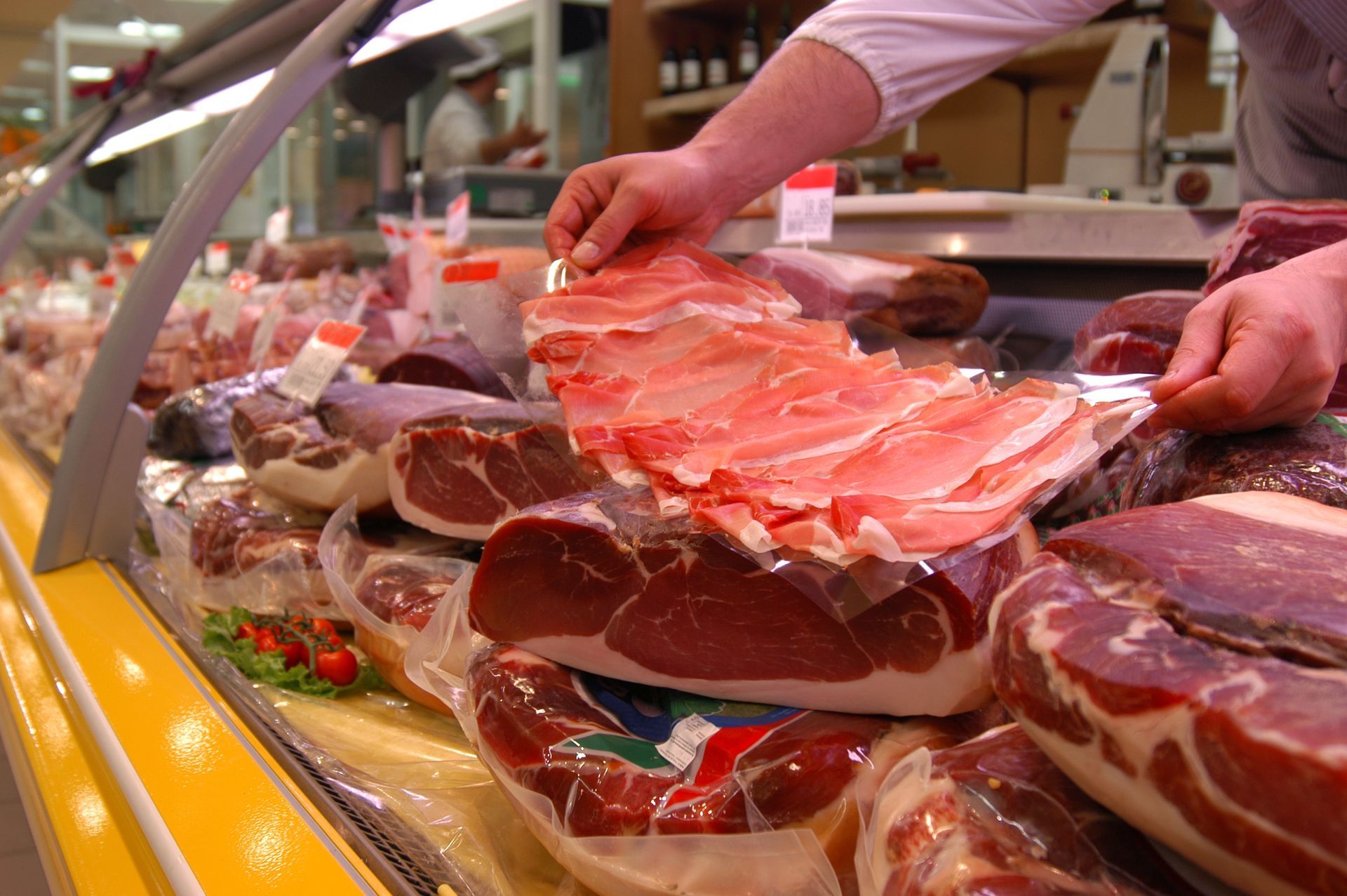 Des mains arrangent des charcuteries sur un comptoir de charcuterie, avec un assortiment de jambons et de salamis tranchés.