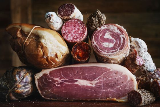 Assortiment de charcuteries et de salami disposés sur une planche en bois, avec un gros jambon tranché devant.