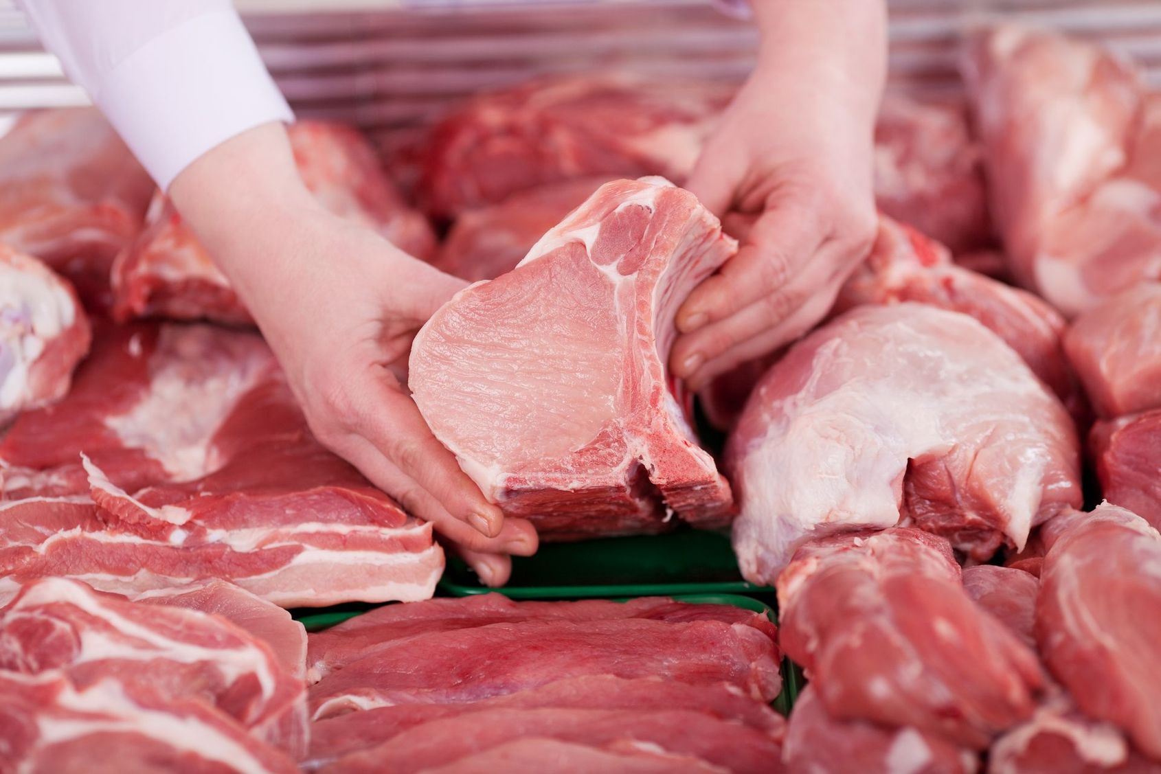Des mains tenant des morceaux de bœuf cru sur le comptoir d'une boucherie, avec diverses viandes rouges en arrière-plan.