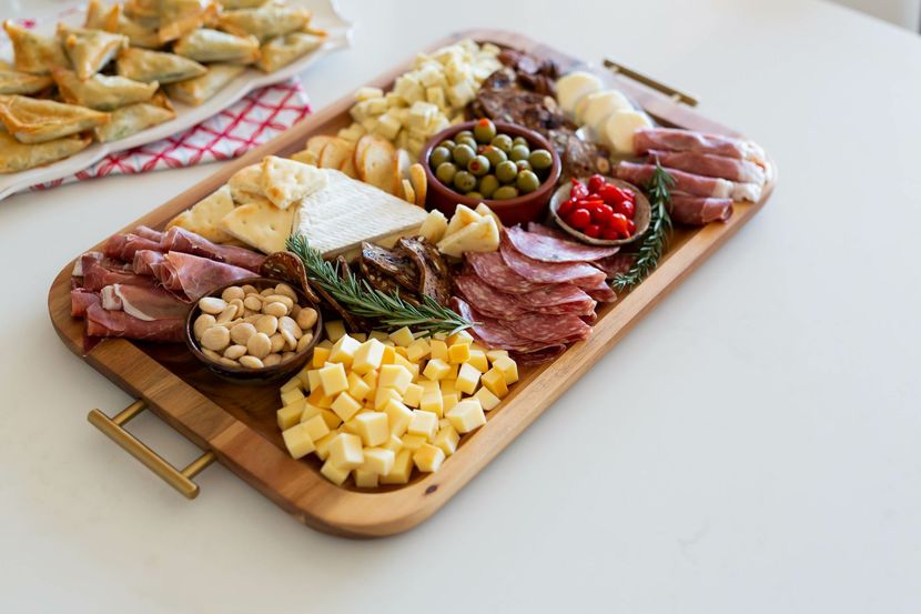 Planche de charcuterie avec fromages, viandes, olives, noix et pain sur une table blanche.