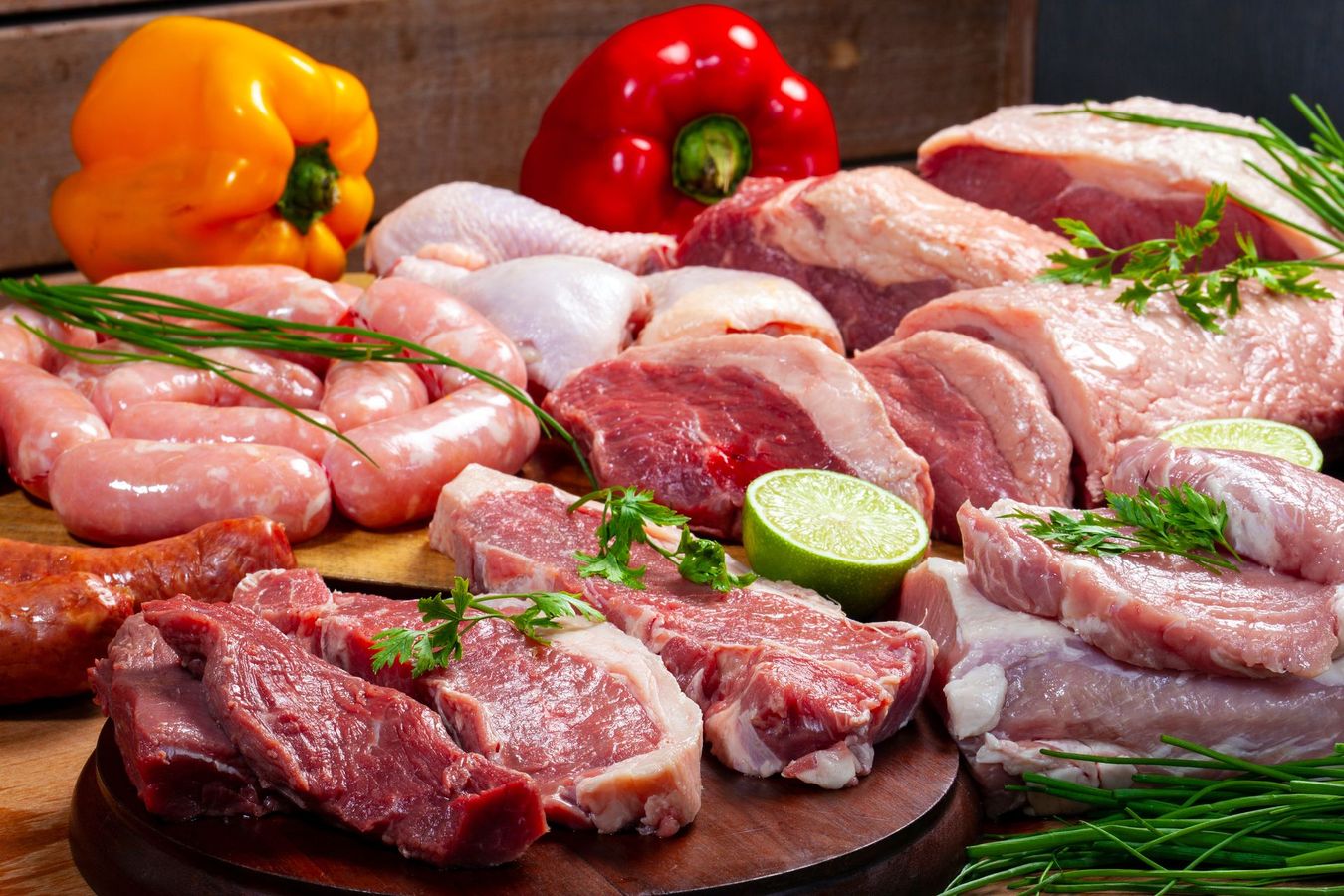 Assortiment de viandes crues et de saucisses avec poivrons et herbes sur un plateau.