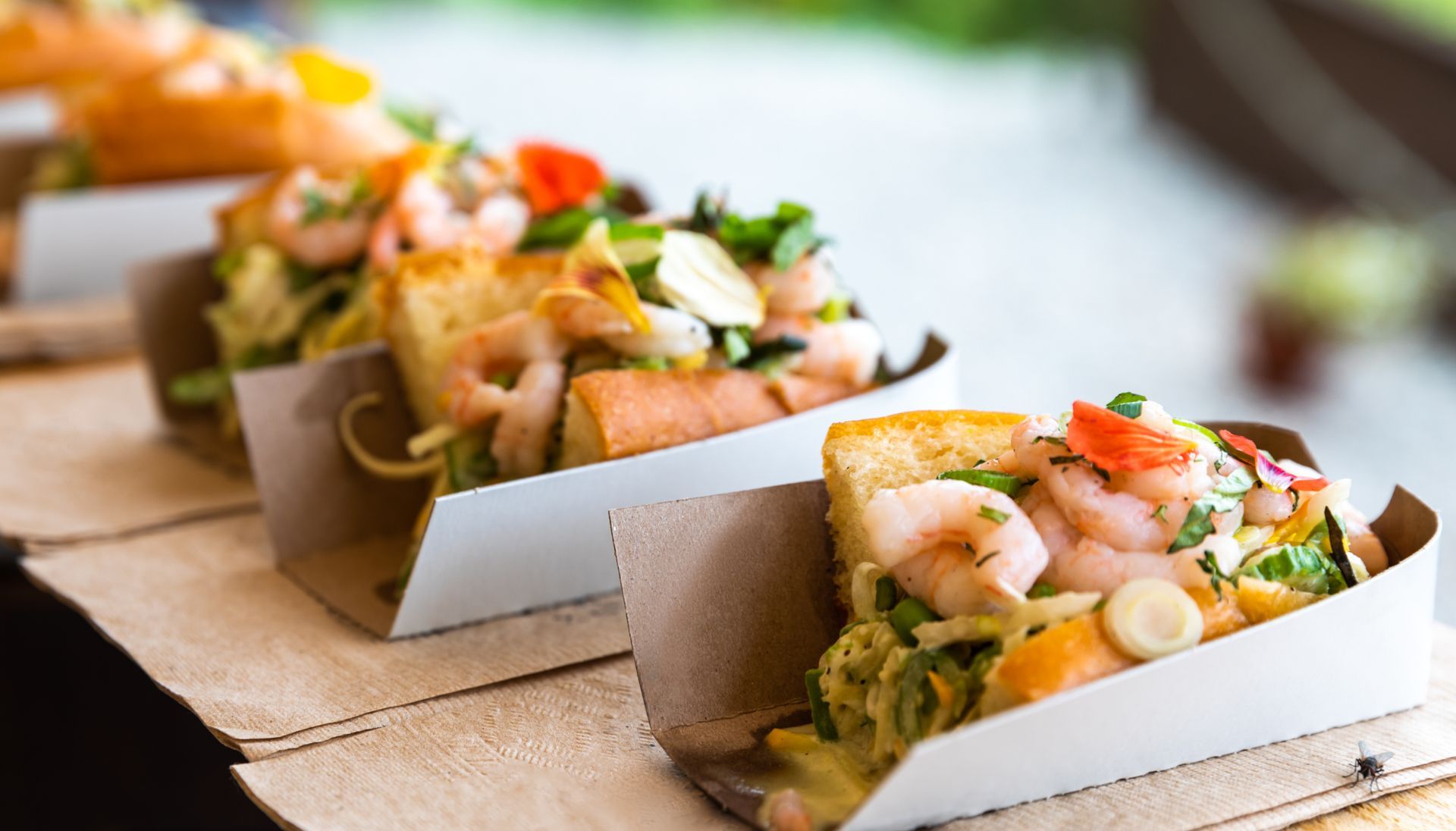 Des boîtes de tacos à emporter avec des crevettes grillées et une garniture fraîche sur une table en bois.