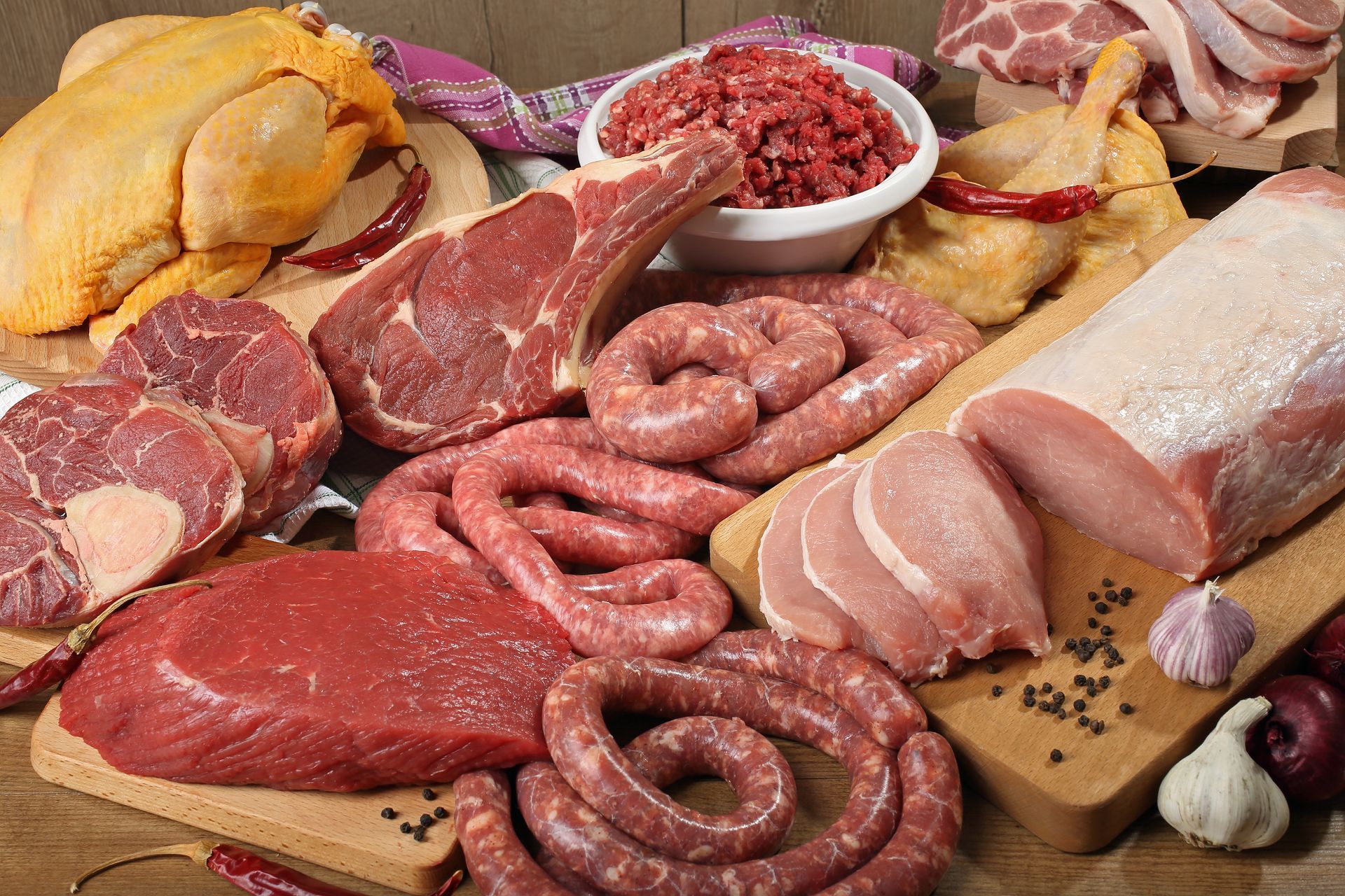 Assortiment de viandes crues et de saucisses disposées sur une table avec du pain et des gousses d'ail.