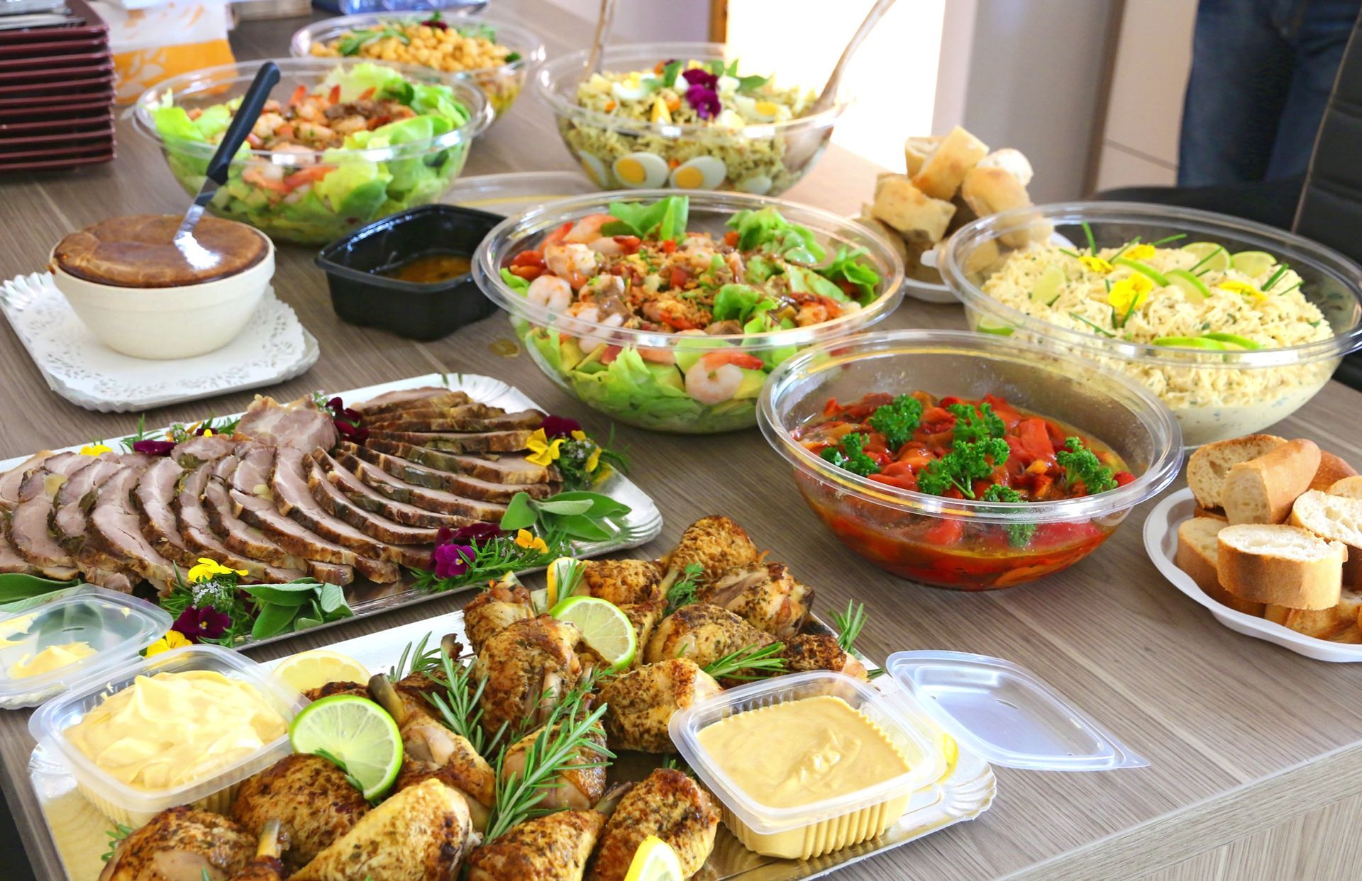 Buffet avec salades, viande rôtie tranchée, pain et sauces, disposé sur une table à manger.
