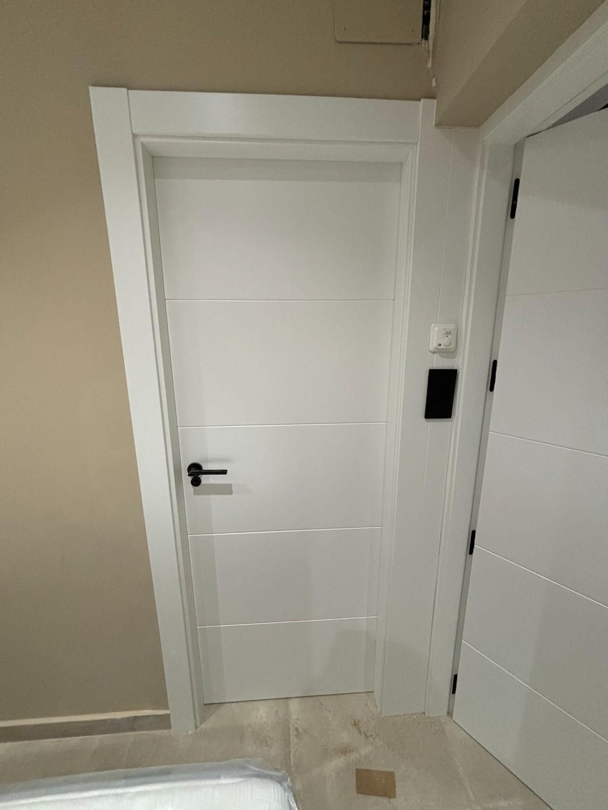 Puerta interior blanca con tirador negro y ranuras horizontales, con marco blanco.