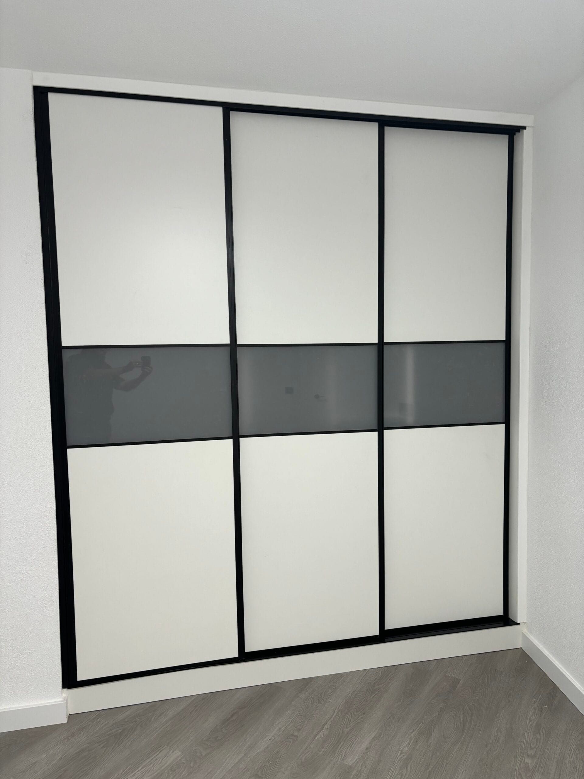 Puertas corredizas de armario: paneles blancos con raya gris y marco negro, en una habitación.