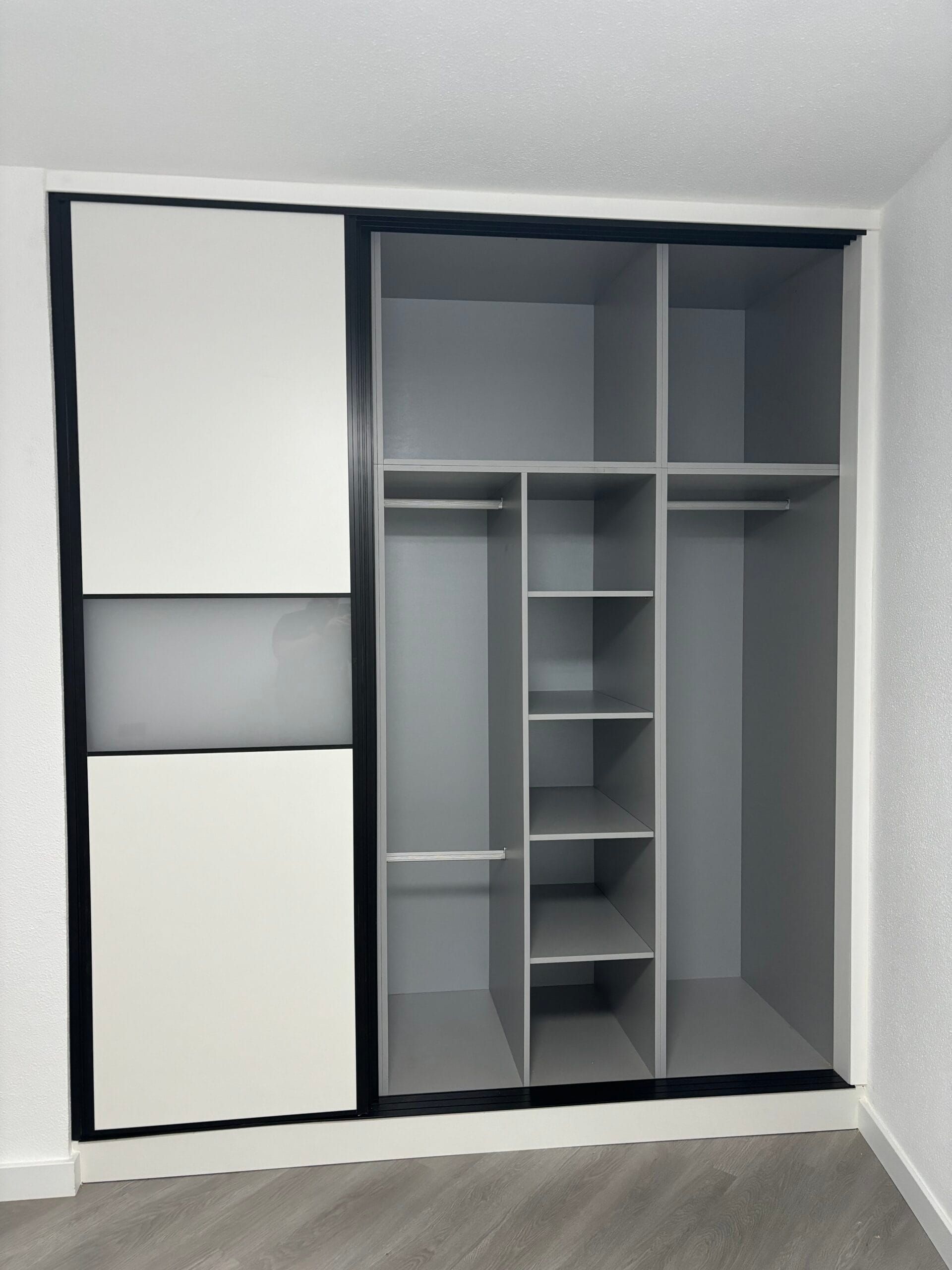 Armario con puertas corredizas de color gris y blanco, con estantes y barras para colgar, apoyado contra una pared blanca.