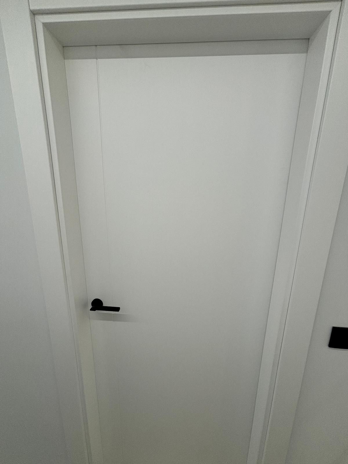 Puerta blanca con tirador negro en marco blanco.
