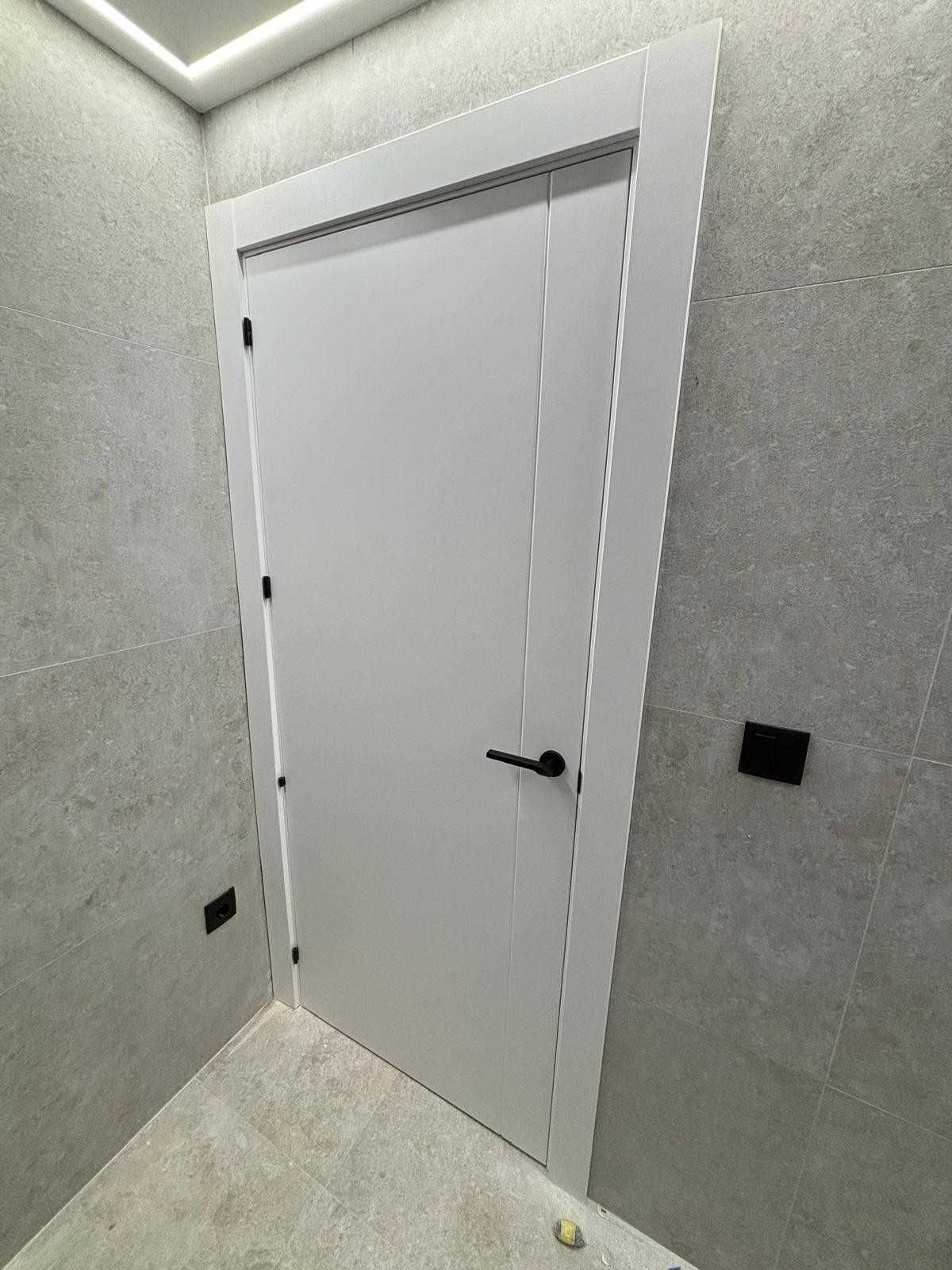 Puerta blanca con manija y moldura de color negro en una habitación con paredes grises texturizadas.