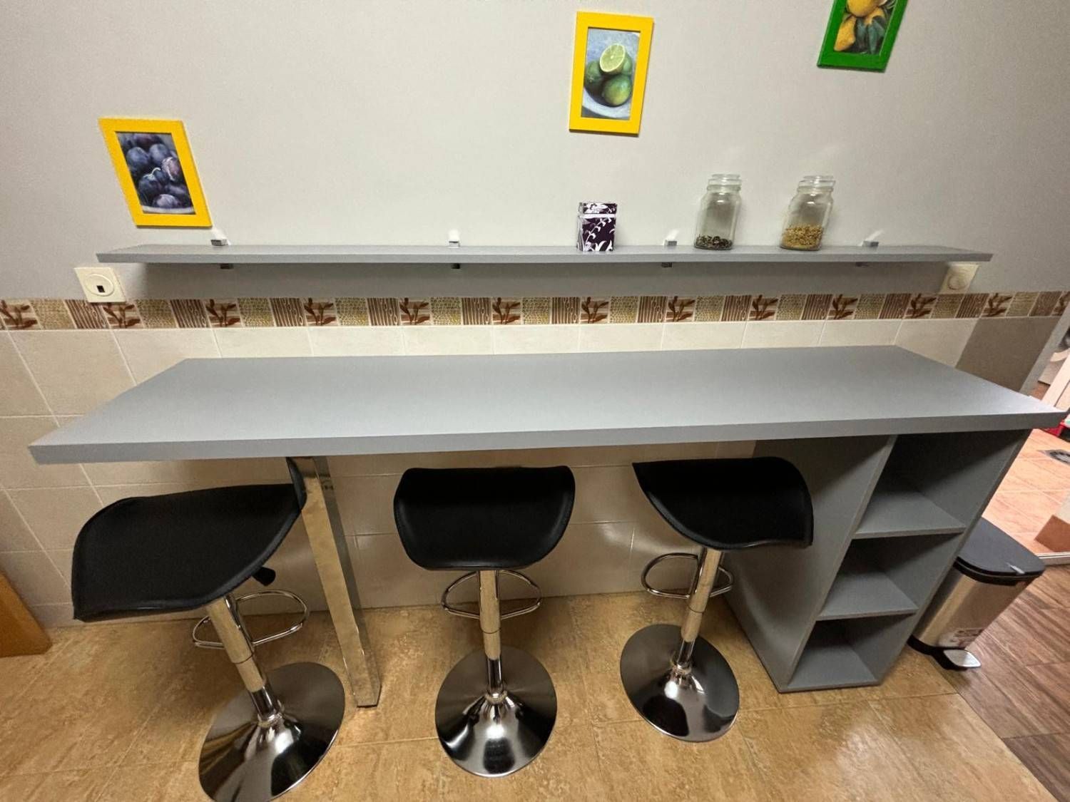 Isla de cocina gris con tres taburetes de bar y un estante contra una pared gris claro.