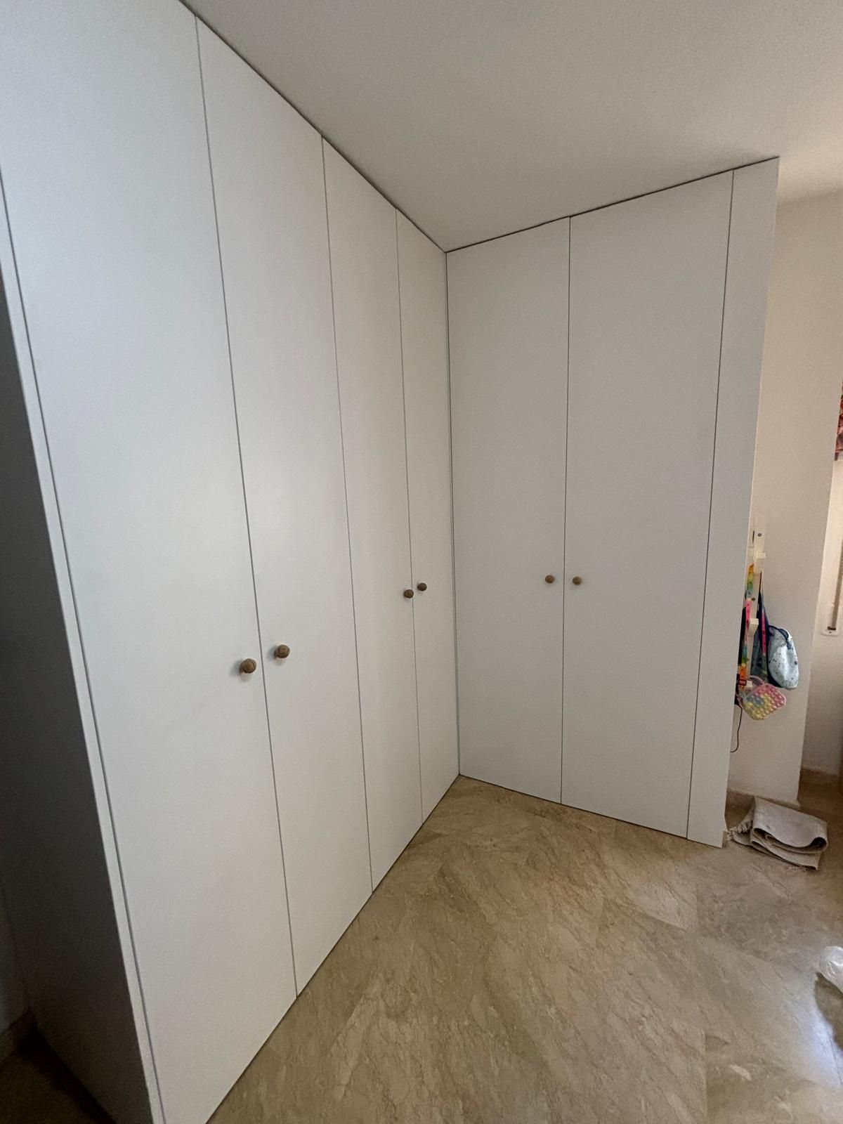 Puertas de armario blancas en un rincón de una habitación, con tiradores redondos sencillos.