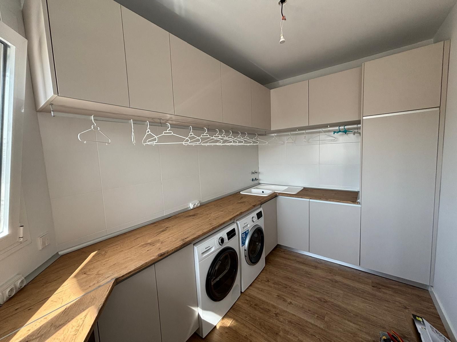 Cuarto de lavado con gabinetes blancos, encimera de madera, lavadora, secadora y tendedero.