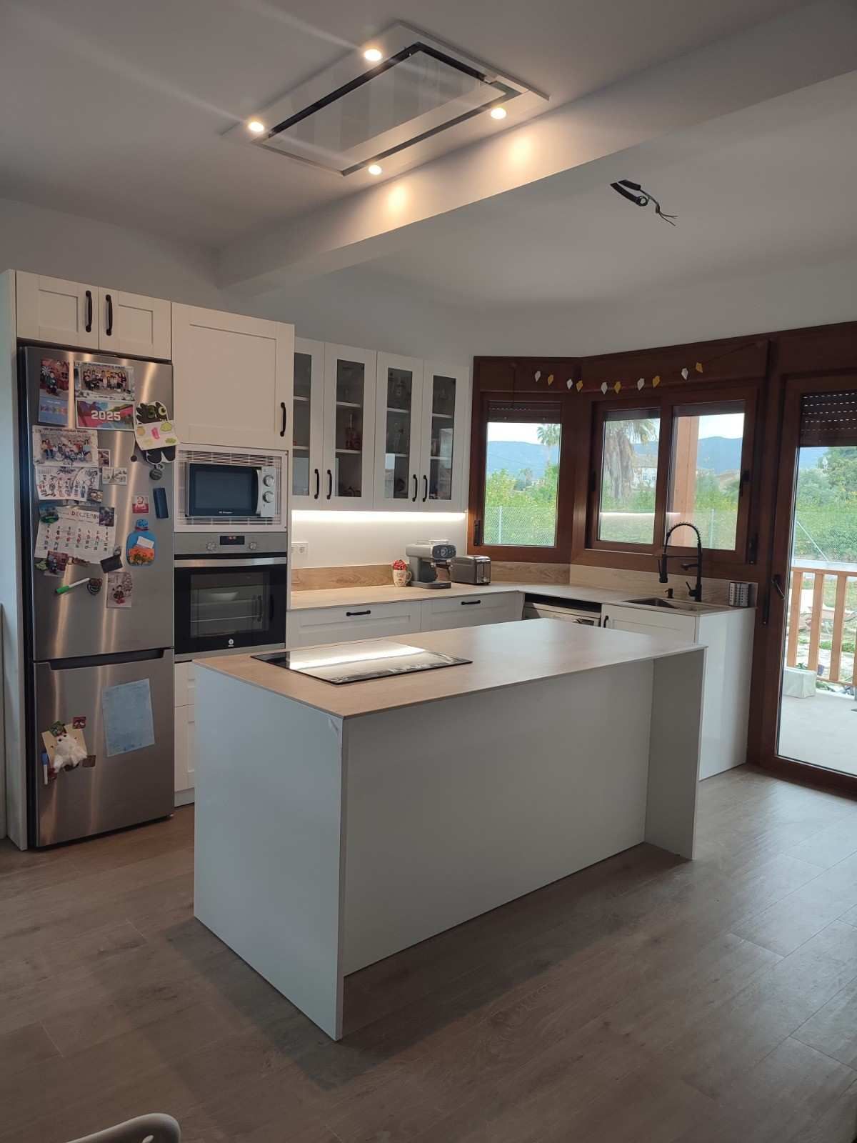 Cocina moderna blanca con isla, electrodomésticos de acero inoxidable y grandes ventanales con vista.