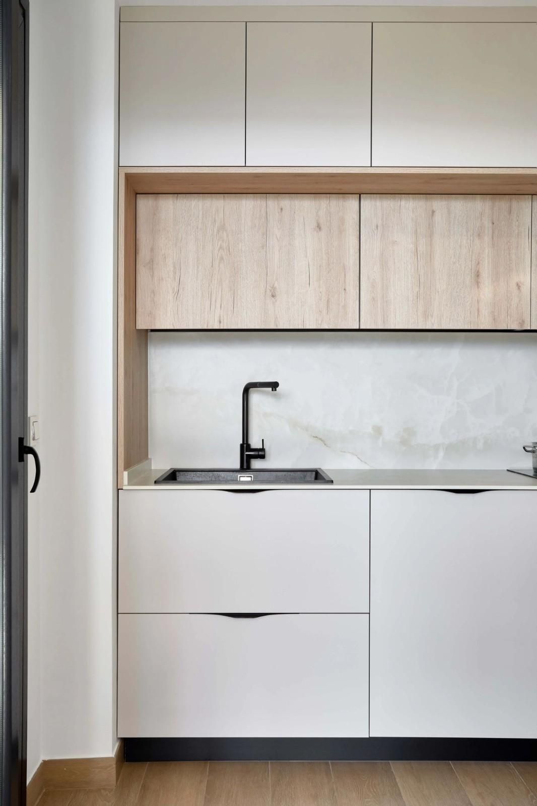 Cocina moderna con gabinetes blancos y de madera, fregadero y grifo negros, salpicadero de mármol.