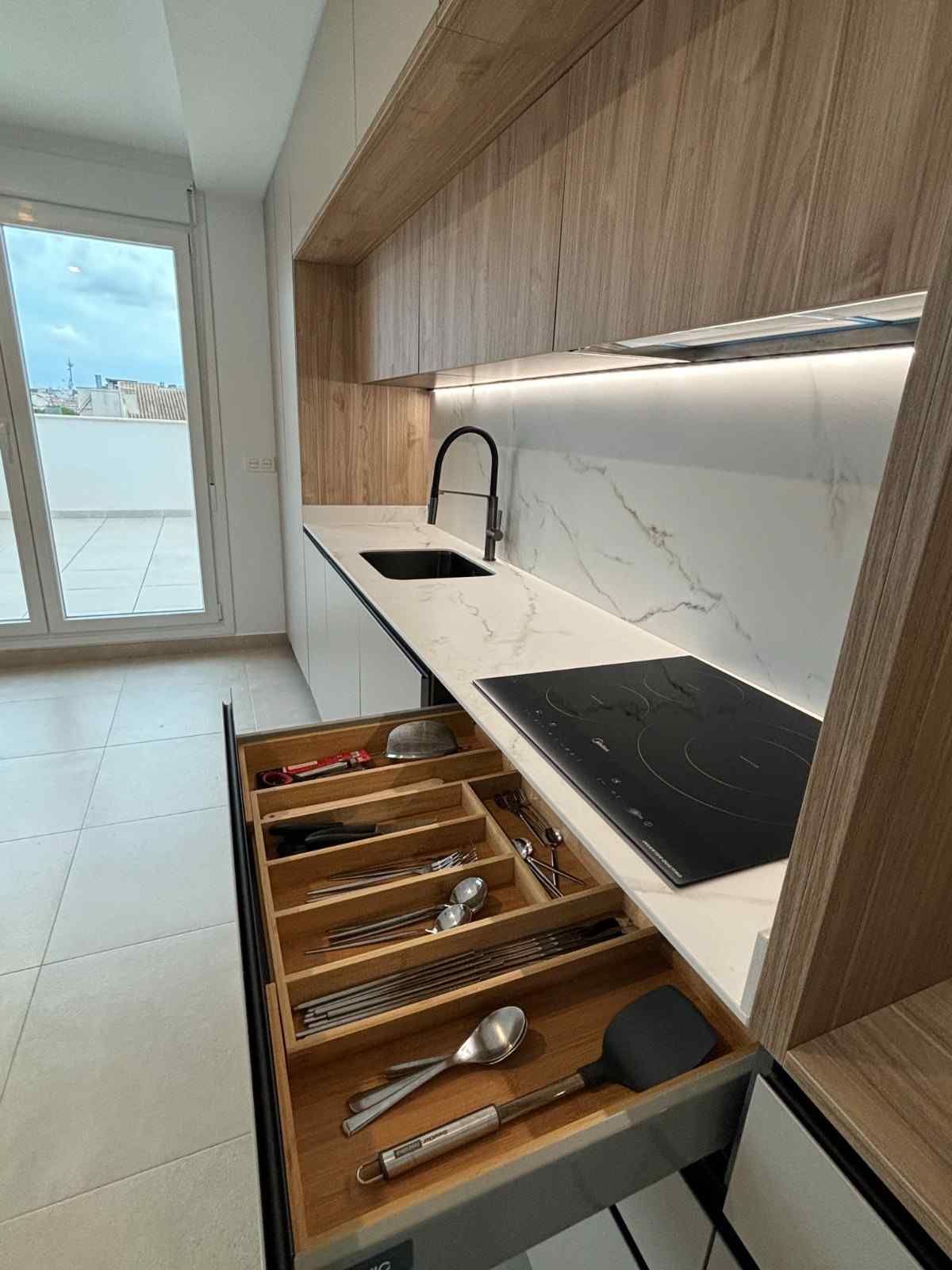 Cocina moderna con gabinetes de madera, protector contra salpicaduras de mármol y un cajón con cubiertos.