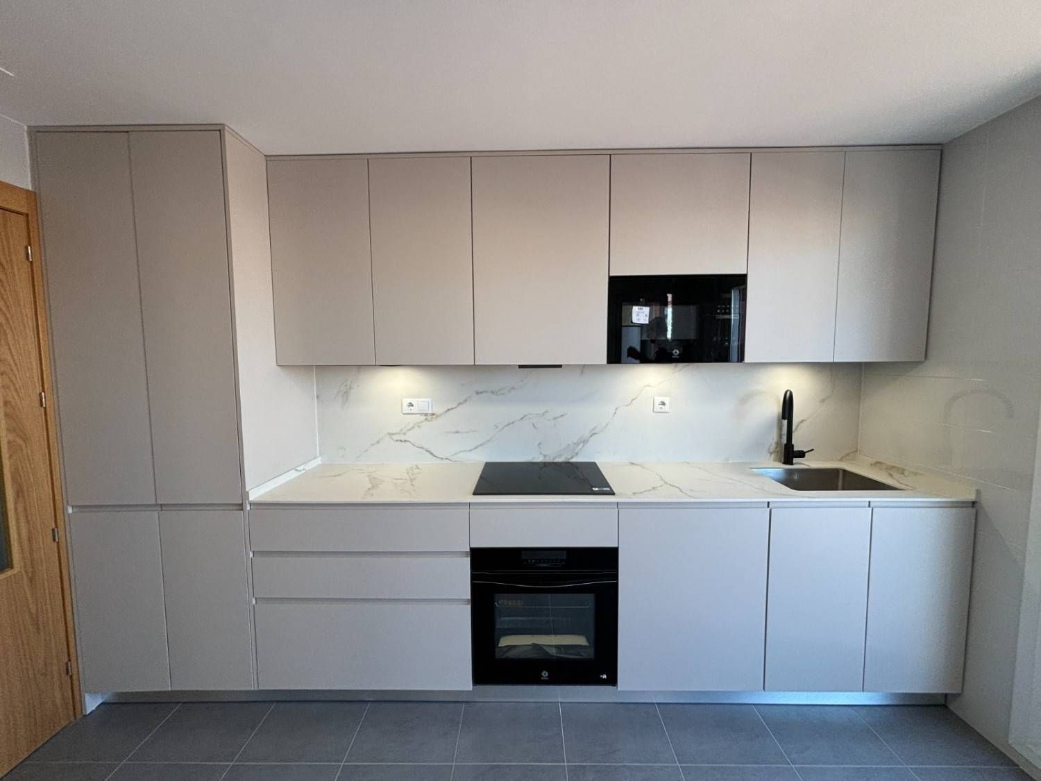 Cocina gris moderna con gabinetes superiores e inferiores, electrodomésticos empotrados.