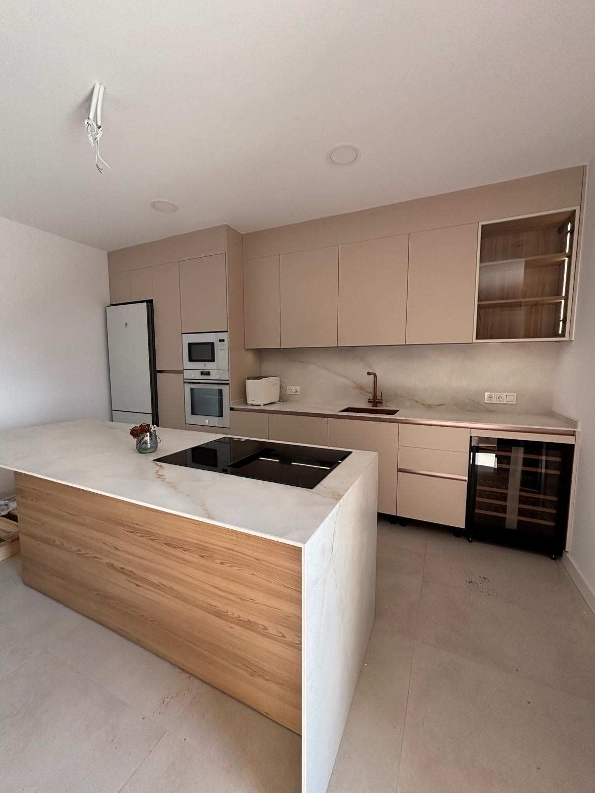 Cocina moderna con gabinetes de color beige claro, isla de encimera blanca y electrodomésticos empotrados.