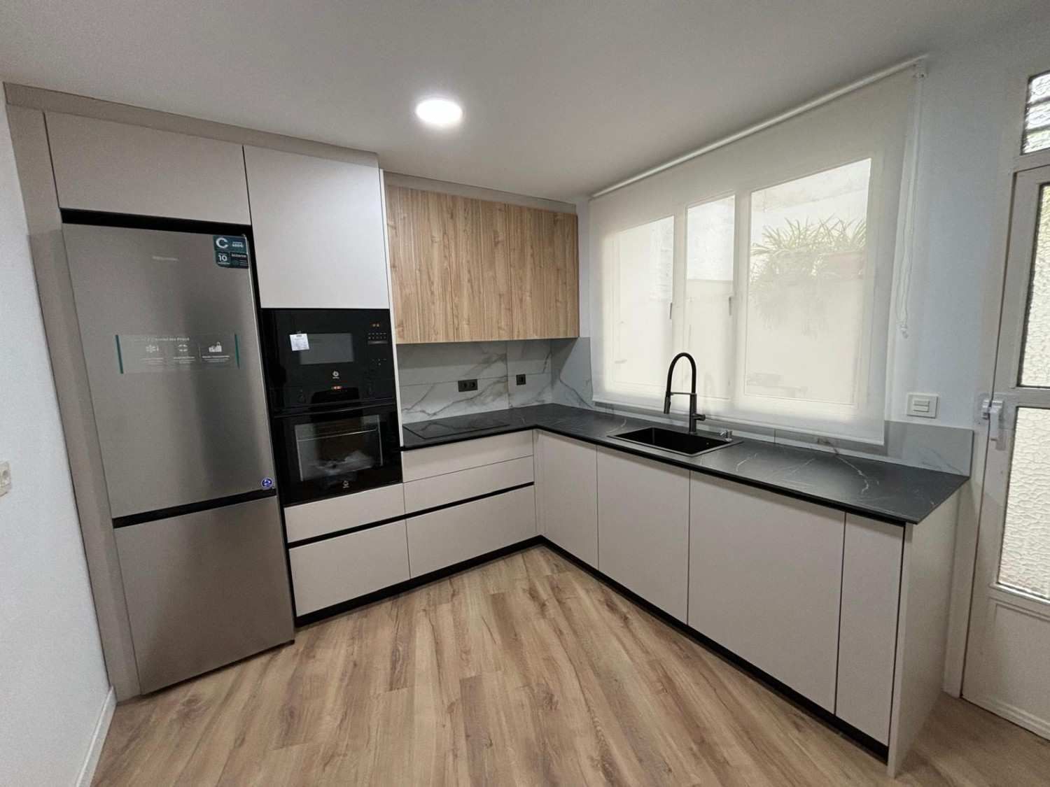 Cocina moderna con electrodomésticos de acero inoxidable, gabinetes de madera clara y encimeras grises.