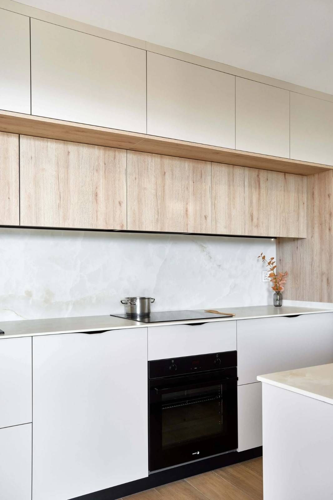 Cocina moderna con gabinetes blancos y de madera, horno negro y salpicadero de mármol.