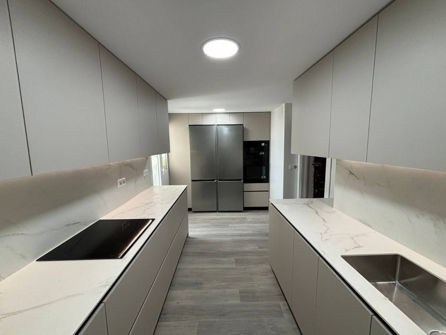 Cocina moderna con gabinetes color gris claro, encimeras blancas y electrodomésticos de acero inoxidable.