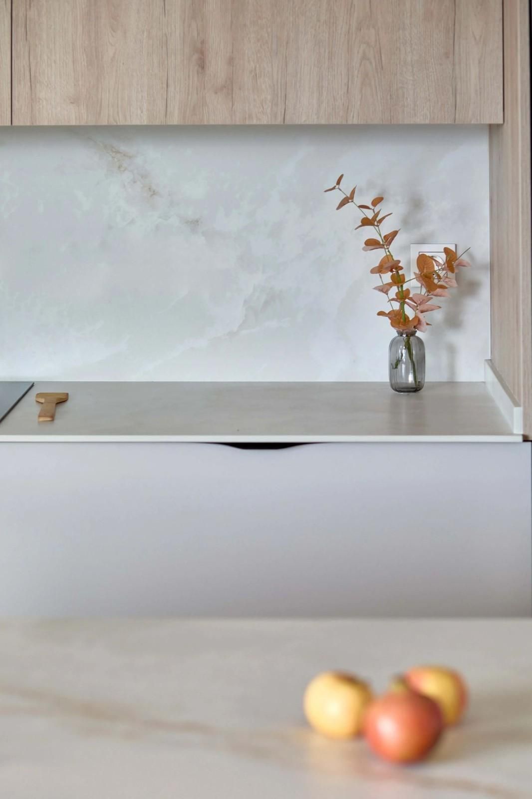 Interior de cocina moderna con salpicadero de mármol, armarios de madera y un jarrón con hojas.