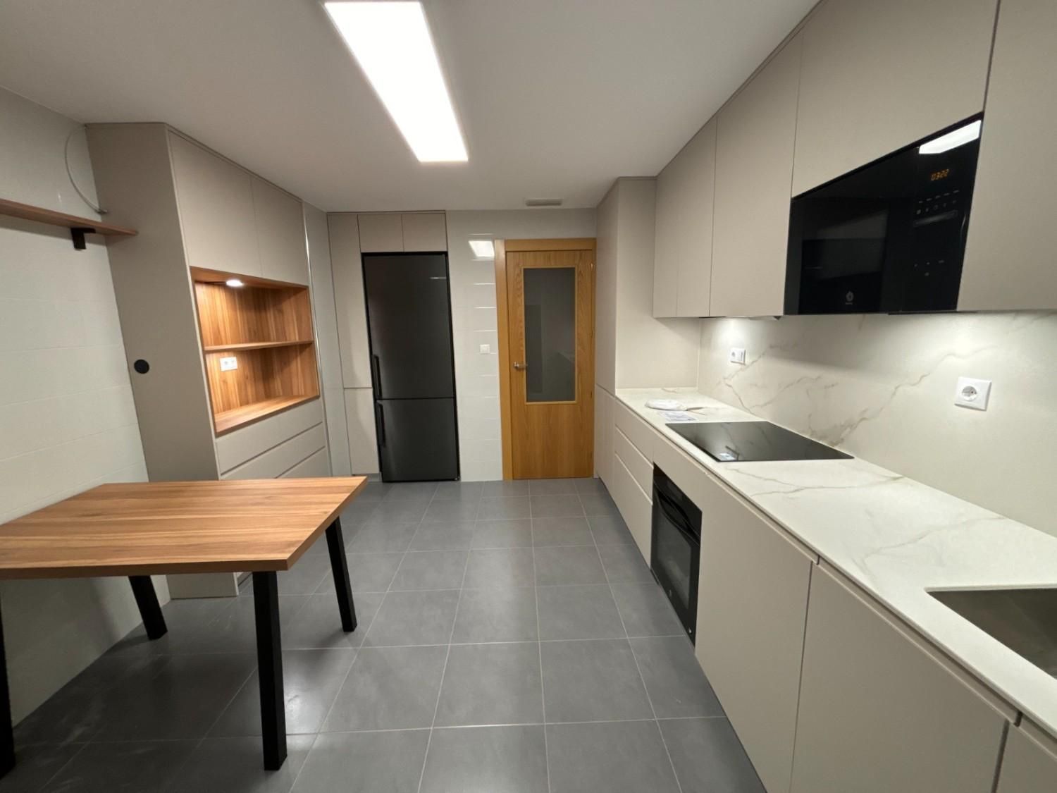 Cocina moderna con gabinetes gris claro, electrodomésticos de acero inoxidable y mesa de madera.