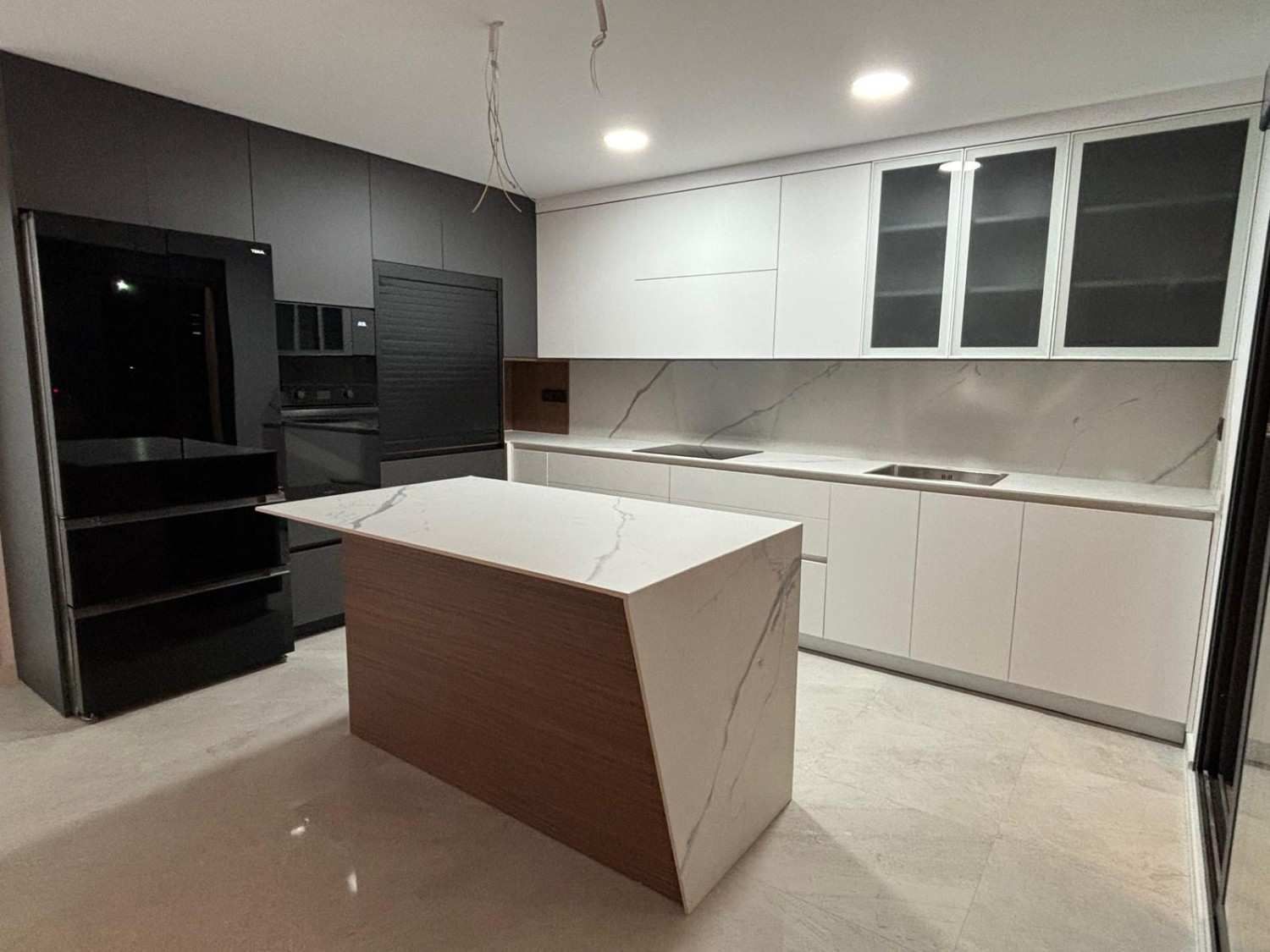 Cocina moderna con gabinetes blancos y oscuros, una isla de encimera y electrodomésticos empotrados.