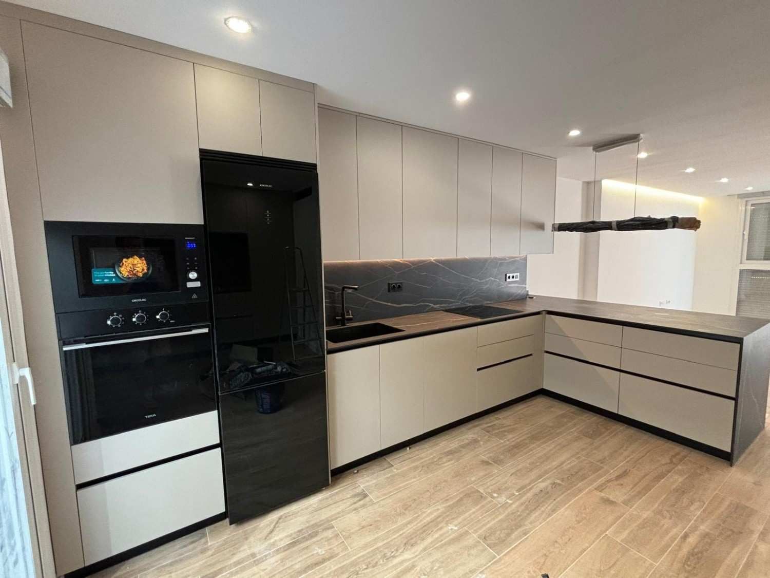Cocina moderna con gabinetes beige, electrodomésticos negros y encimera gris.