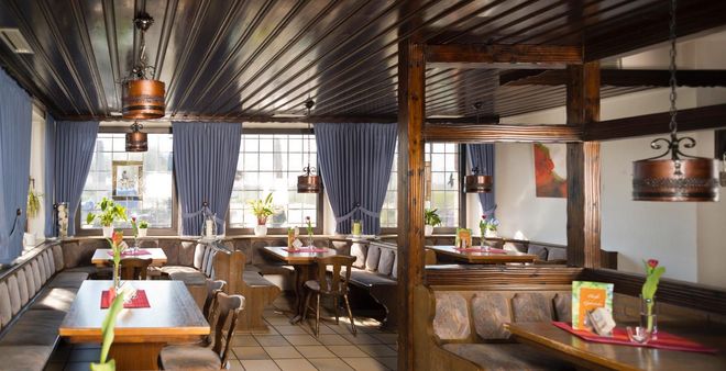 Gemütliches Restaurantinterieur mit Holzbalken, gedeckten Tischen und blauen Vorhängen an den Fenstern.
