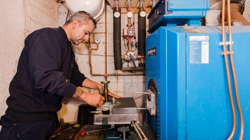 Ein Mann arbeitet in einem Keller an einem blauen Heizkessel.