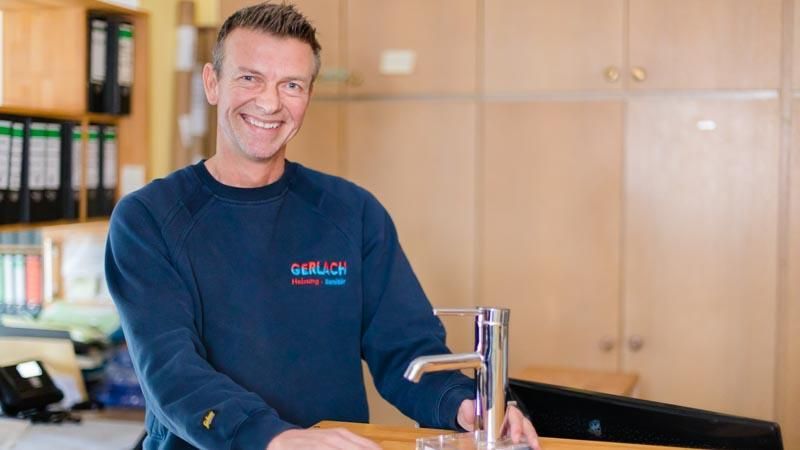 Ein Mann in einem blauen Pullover steht neben einem Wasserhahn.