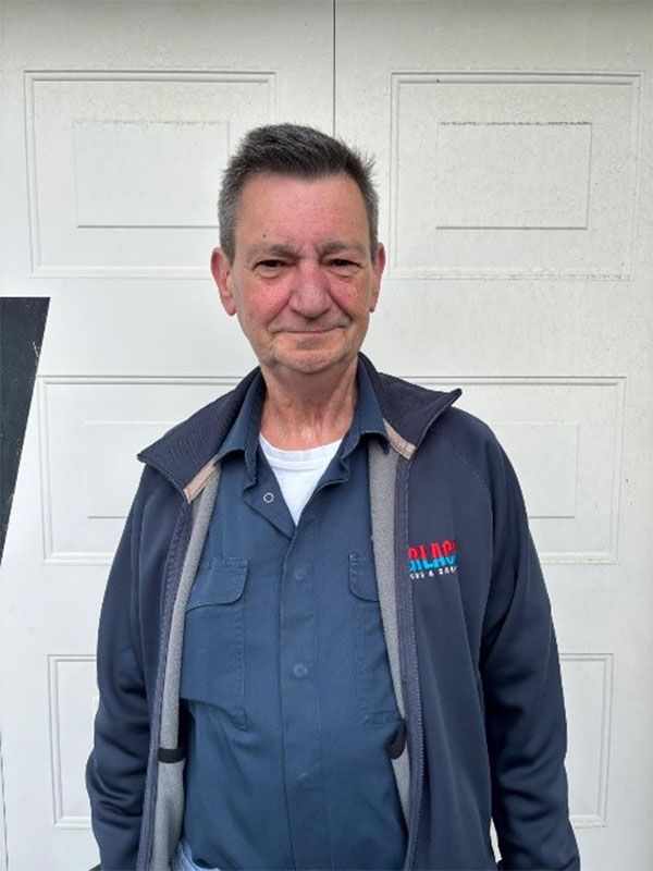 Ein Mann mit blauem Hemd und blauer Jacke steht vor einem weißen Garagentor.