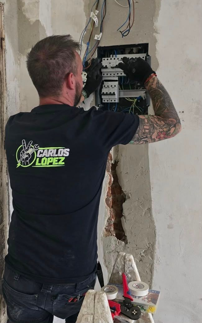 Un trabajador instala un cuadro eléctrico en una pared dañada, usando herramientas en el interior.