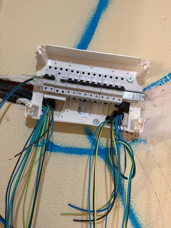 Cuadro eléctrico con cables verdes y azules al descubierto en una pared