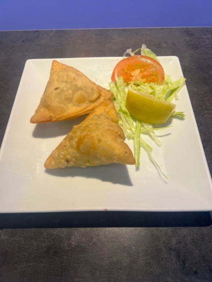 Deux samoussas dorés sur une assiette blanche, garnis de laitue, de tomate et d'une tranche de citron