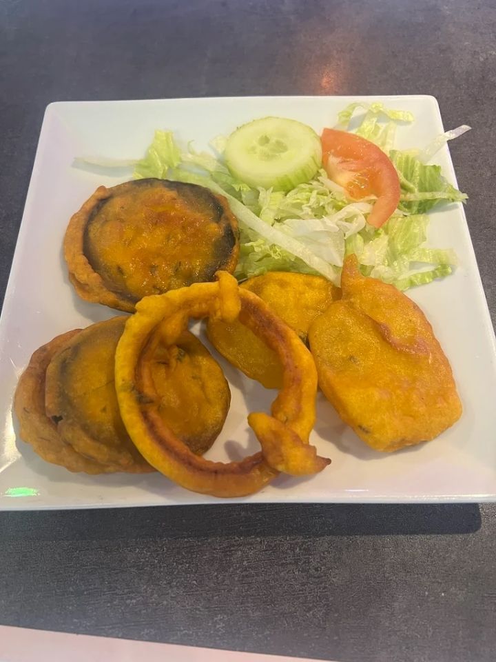 Assiette de samoussas garnie de salade, tomate et concombre posée sur un plan de travail gris