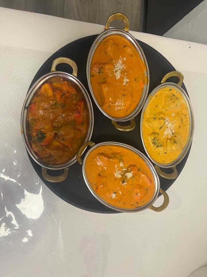 Quatre petits bols de curry coloré disposés sur un plateau rond noir, vus de dessus.