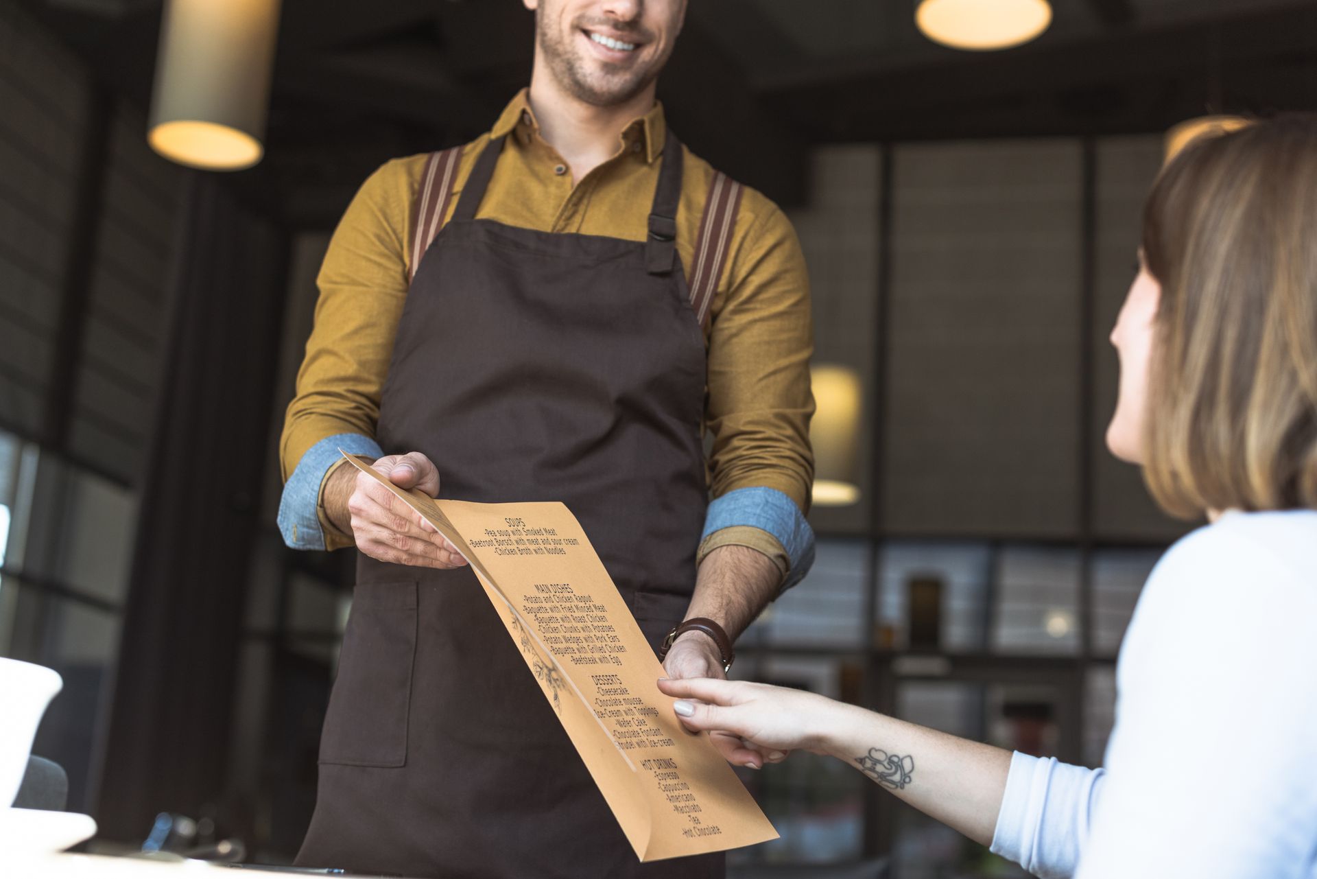 Serveur de restaurant présentant une carte à une cliente assise à une table.