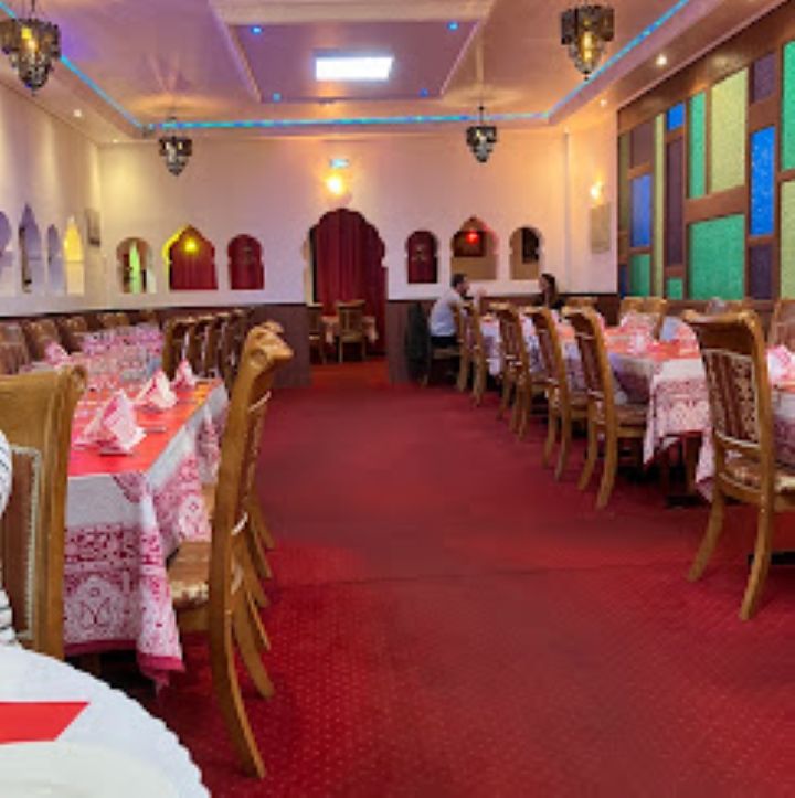 Salle de banquet vide avec moquette rouge, nappes à motifs, chaises en bois et panneaux muraux colorés