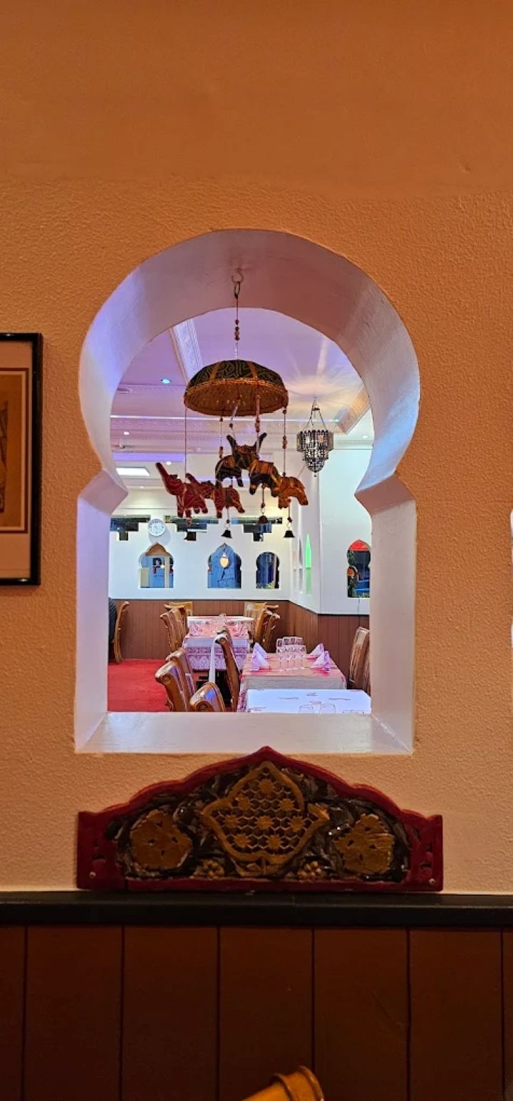 Une ouverture cintrée dans le mur dévoile une salle à manger baignée d'une lumière chaleureuse, ornée de décorations suspendues et d'une table dressée en rouge.