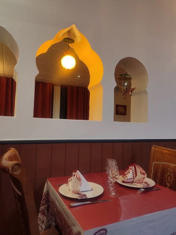 Banquette de restaurant confortable avec nappe rouge, tables dressées, niches murales cintrées et luminaires suspendus à l'ambiance chaleureuse.