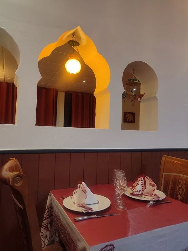 Banquette de restaurant confortable avec nappe rouge, assiettes dressées et niches murales cintrées éclairées par des suspensions lumineuses à la lumière chaude.
