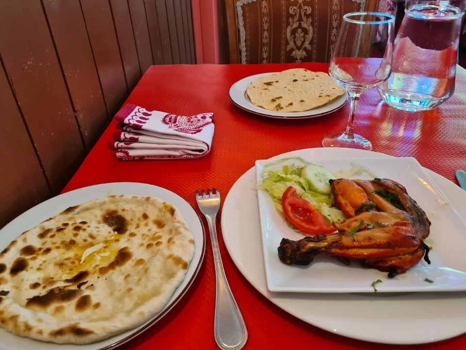 Poulet grillé et pains plats disposés sur une table rouge avec un verre et une carafe à eau dans un restaurant