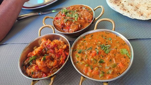 Trois bols de curry rouge orangé garnis d'herbes aromatiques, disposés sur une nappe grise.