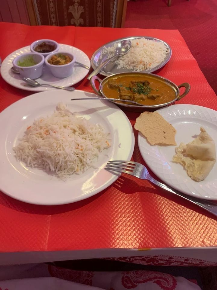 Repas indien sur une nappe rouge avec riz, curry, chutneys, naan et papadums dans des assiettes blanches
