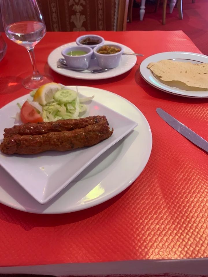 Table de restaurant avec viande grillée, salade, sauces, verre d'eau et pain sur une nappe rouge