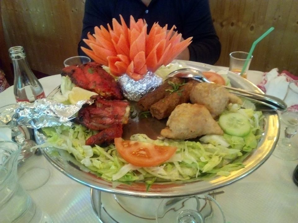 Plateau décoré de grillades et de salade sur une table, avec une garniture de carotte en forme de fleur et des éléments en papier aluminium.
