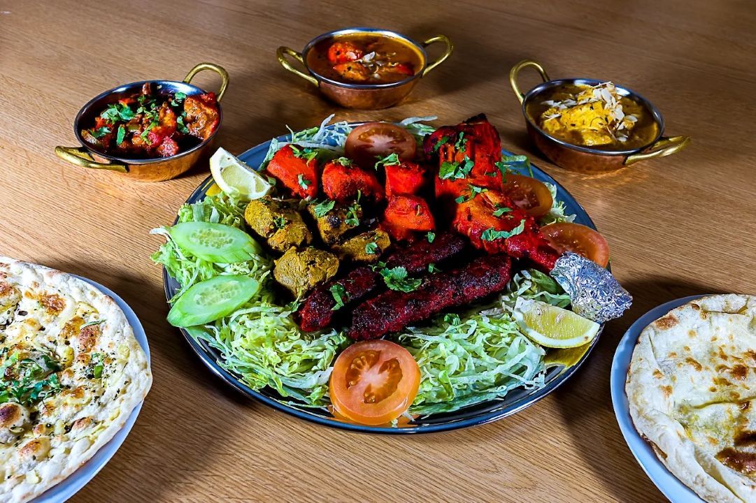 Assortiment de brochettes grillées dans un grand plat, accompagné de salade et de garnitures sur une table