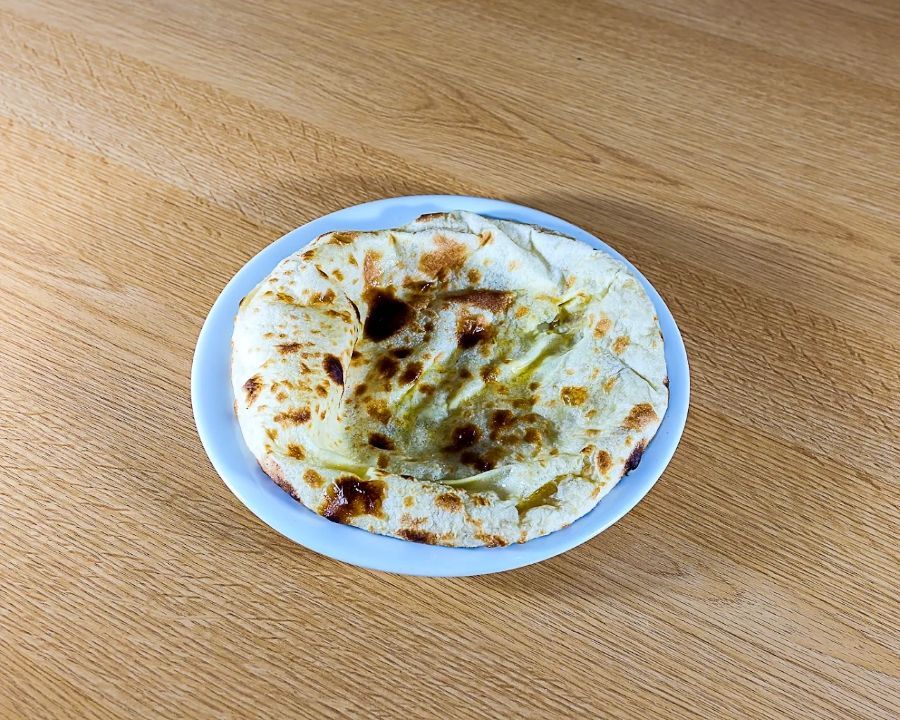 Assiette blanche avec un naan sur une table en bois